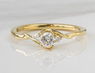 A yellow gold solitaire engagement ring with a round-cut center stone and small side stones, displayed on a reflective white surface.