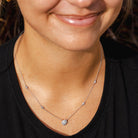 A close-up lifestyle shot of a woman wearing a delicate silver necklace with a small round pavé pendant and small accent beads, paired with a black shirt.